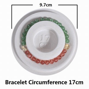 May include: A white foam bracelet sizing ring with a 17 cm circumference. The ring has three rows of beads: green, gold, and red.