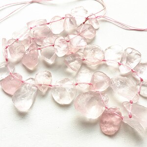 May include: A strand of pink rose quartz beads strung on pink thread. The beads are irregular in shape and have a translucent appearance.