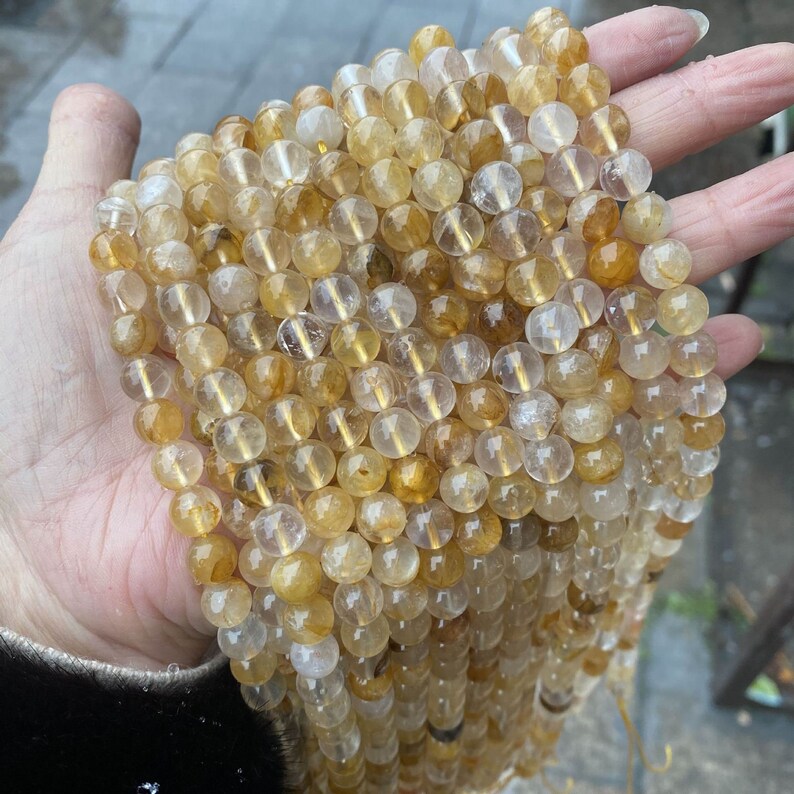 K&ouml;nnte beinhalten: Eine Str&auml;hne runder, durchscheinender, goldener Citrinperlen. Die Perlen haben einen Durchmesser von etwa 8 mm und eine nat&uuml;rliche, facettierte Oberfl&auml;che.
