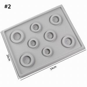 May include: A gray silicone mold with eight circular depressions of different sizes, labeled with their diameter in centimeters. The mold measures 26 cm by 34 cm.