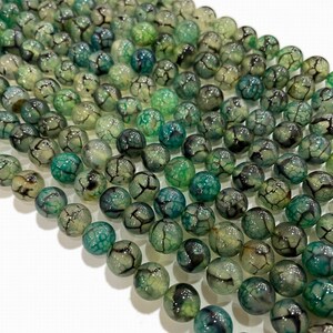 May include: A selection of green and teal spherical beads featuring a cracked, web-like design. The beads display varying shades, giving a textured and natural look. These beads are suitable for jewellery making.