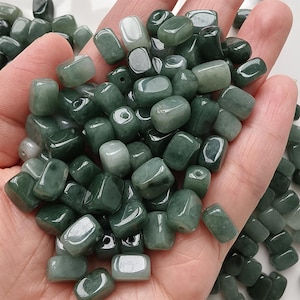 Puede incluir: Un puñado de cuentas de jade pulidas de color verde oscuro. Las cuentas son lisas, rectangulares y tienen un acabado brillante. El color varía de un verde bosque profundo a tonos más claros, con algunas cuentas que parecen casi translúcidas.