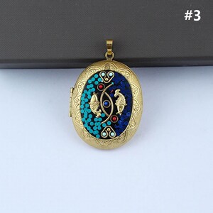 May include: A gold oval locket with a blue and turquoise mosaic design featuring two gold fish. The locket has a hinge on the side and a loop at the top for attaching a chain.