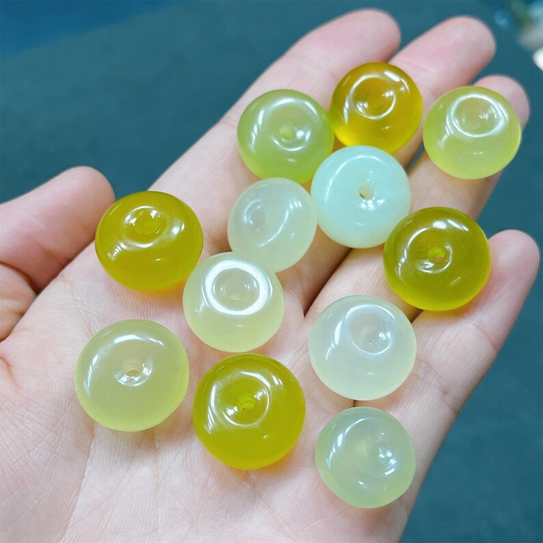May include: A collection of 13 green and yellow jade donut beads. The beads are smooth and polished, with a hole in the center of each bead.