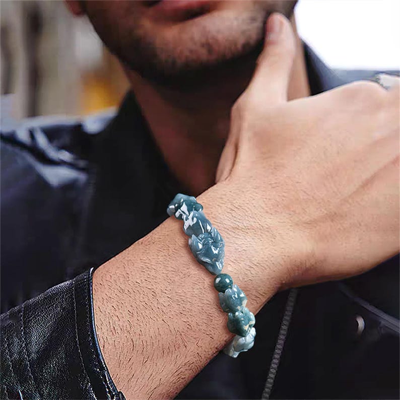 Puede incluir: Un brazalete de jade con un dise&ntilde;o tallado. El brazalete presenta una serie de piezas de jade verde claro y verde oscuro conectadas. El brazalete se usa en la mu&ntilde;eca.