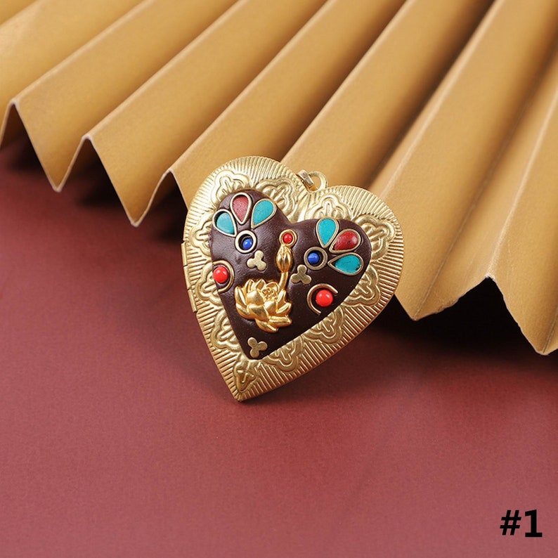 Puede incluir: Un medall&oacute;n de coraz&oacute;n de oro con un dise&ntilde;o intrincado y acentos de esmalte de colores. El medall&oacute;n presenta un motivo floral con acentos rojos, azules y turquesa.