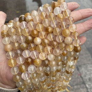 K&ouml;nnte beinhalten: Eine Str&auml;hne runder, durchsichtiger Perlen in goldgelber Farbe. Die Perlen sind auf einem durchsichtigen Faden aufgereiht. Die Perlen haben einen Durchmesser von etwa 8 mm.