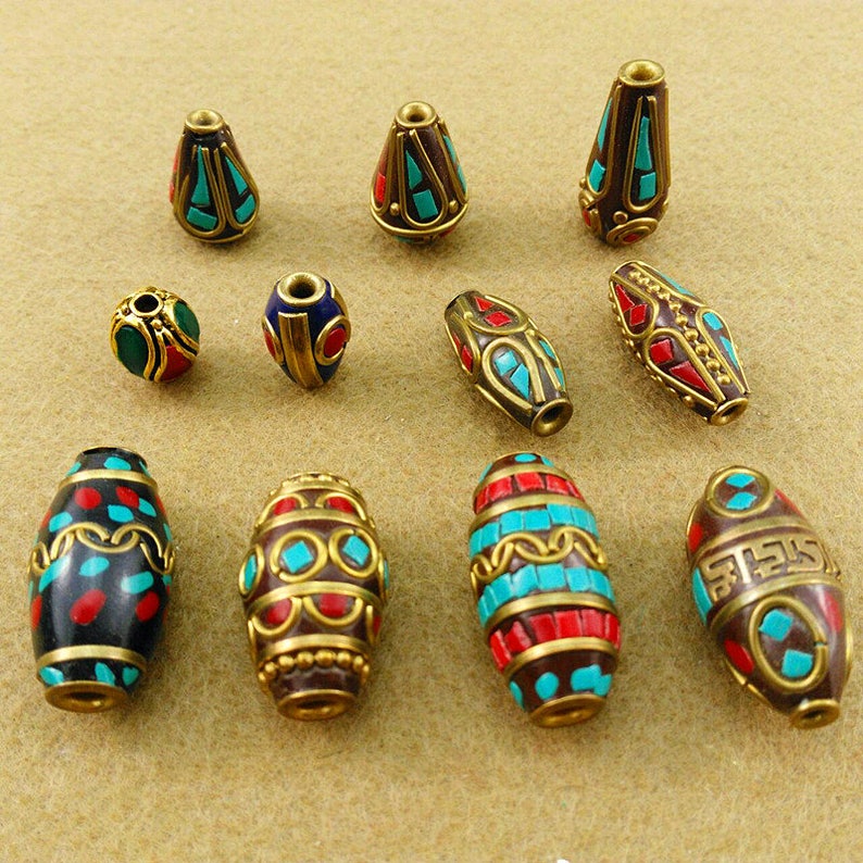 May include: Assortment of colorful, ornate beads with intricate designs. The beads are made of metal and feature turquoise, red, and gold accents.
