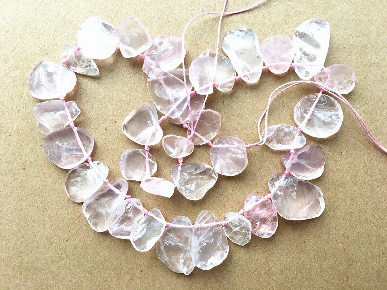 May include: A strand of light pink and clear gemstone beads, strung on pink thread. The beads are irregularly shaped and have a translucent appearance.