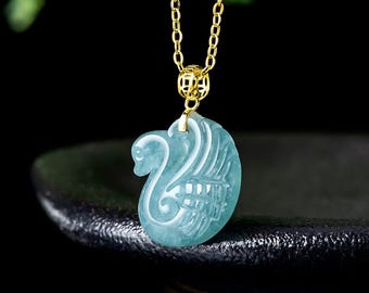May include: A light blue, translucent, carved stone pendant in the shape of a swan, suspended from a thin gold-colored metal chain. The pendant features detailed etched lines forming the swan's neck and wing, attached by a small gold-toned bail.
