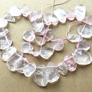 May include: A strand of clear and pale pink gemstone beads, strung on pink thread. The beads are irregularly shaped and have a smooth, polished finish.