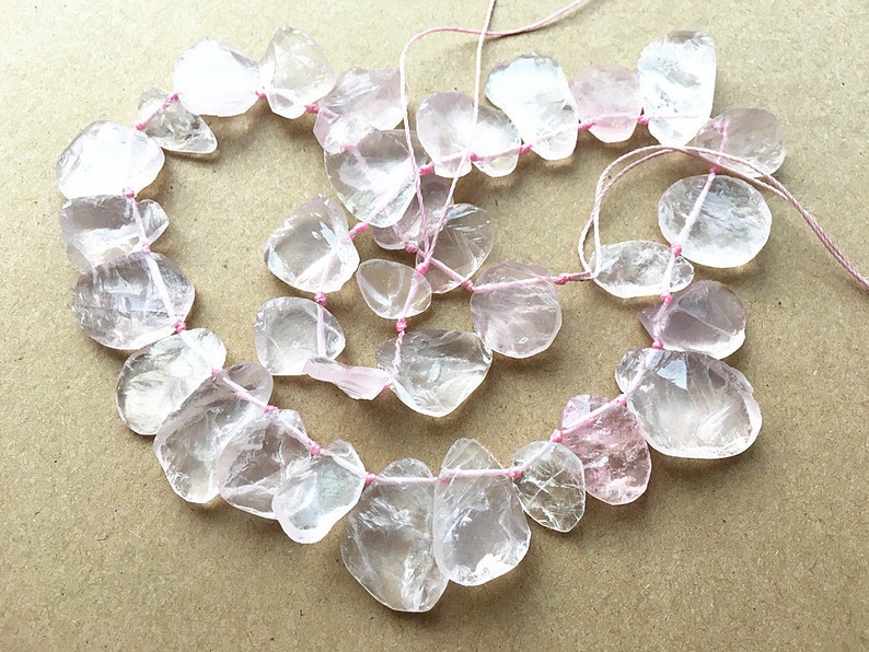May include: A strand of clear and pale pink gemstone beads, strung on pink thread. The beads are irregularly shaped and have a smooth, polished finish.