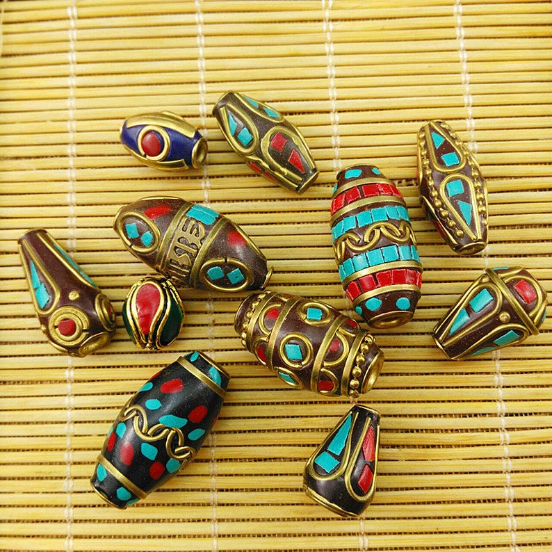 May include: Assortment of oval-shaped beads with intricate designs. The beads are made of dark brown wood with turquoise and red enamel accents. Some beads have gold-colored metal accents.