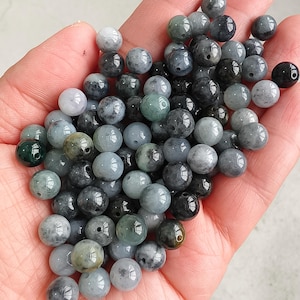 May include: A collection of round beads in shades of grey, green, and black. The beads have a glossy finish and are drilled for stringing. The colours vary from light grey to dark grey and green. Ideal for jewellery making or crafts.
