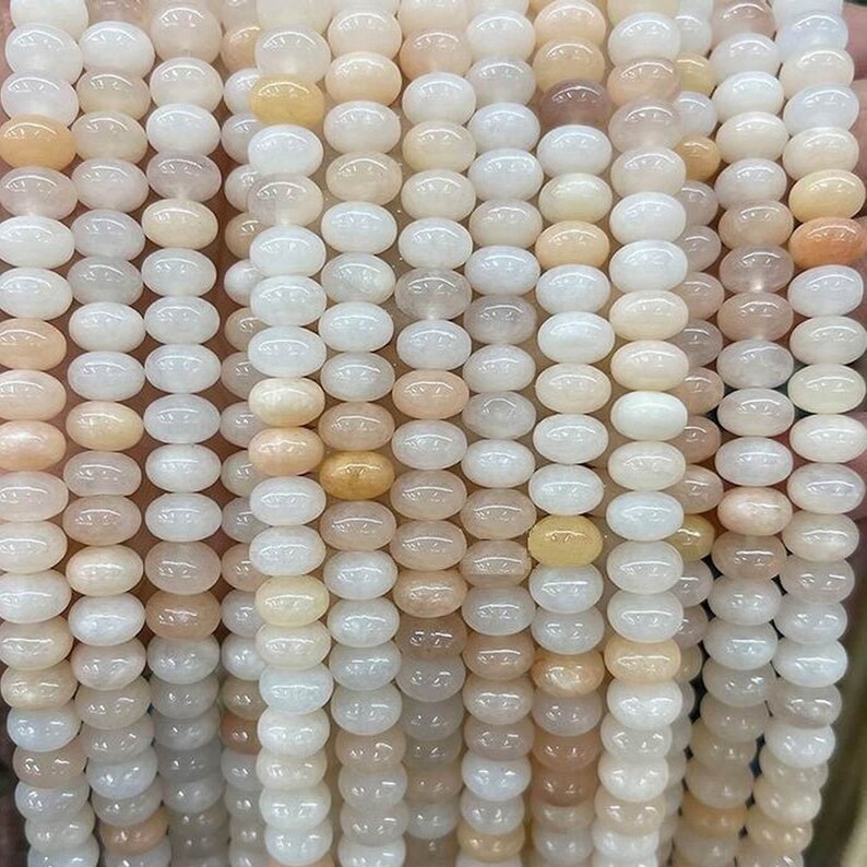 May include: A strand of white and peach colored oval-shaped beads. The beads are smooth and glossy.