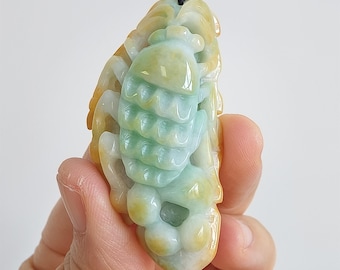 May include: A jade pendant carved in the shape of a stylized insect. The pendant features a blend of colors, including yellow, green, and white. It is suspended from a black cord with a small, round, light green bead.