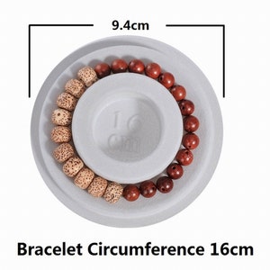 May include: A wooden beaded bracelet with brown and beige beads, displayed on a white circular platform with a 16cm diameter. The bracelet is 9.4cm in diameter.