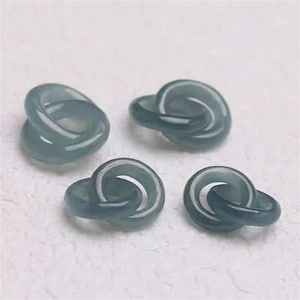 Könnte beinhalten: Vier Jadeit-Jade-Ringe, jeder mit einem Doppel-Schleifendesign. Die Ringe sind in einem blassblaugrünen Farbton gehalten und haben eine glatte, polierte Oberfläche.