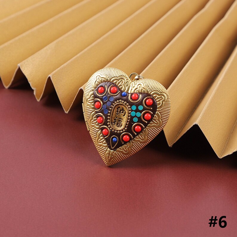 Puede incluir: Un medall&oacute;n de coraz&oacute;n de oro con un dise&ntilde;o detallado y acentos coloridos. El medall&oacute;n tiene una peque&ntilde;a abertura en el lateral para una cadena.