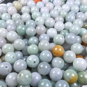 May include: A collection of round, smooth jade beads in various shades of green, white, and yellow. The beads are all approximately the same size and have a polished finish.