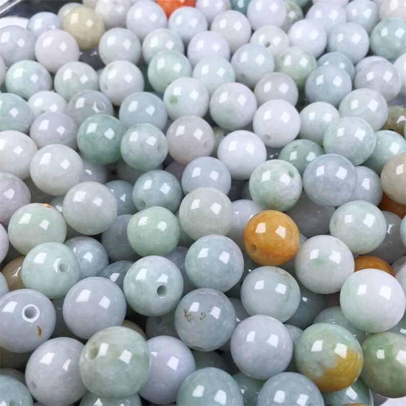 May include: A collection of round, smooth jade beads in various shades of green, white, and yellow. The beads are all approximately the same size and have a polished finish.