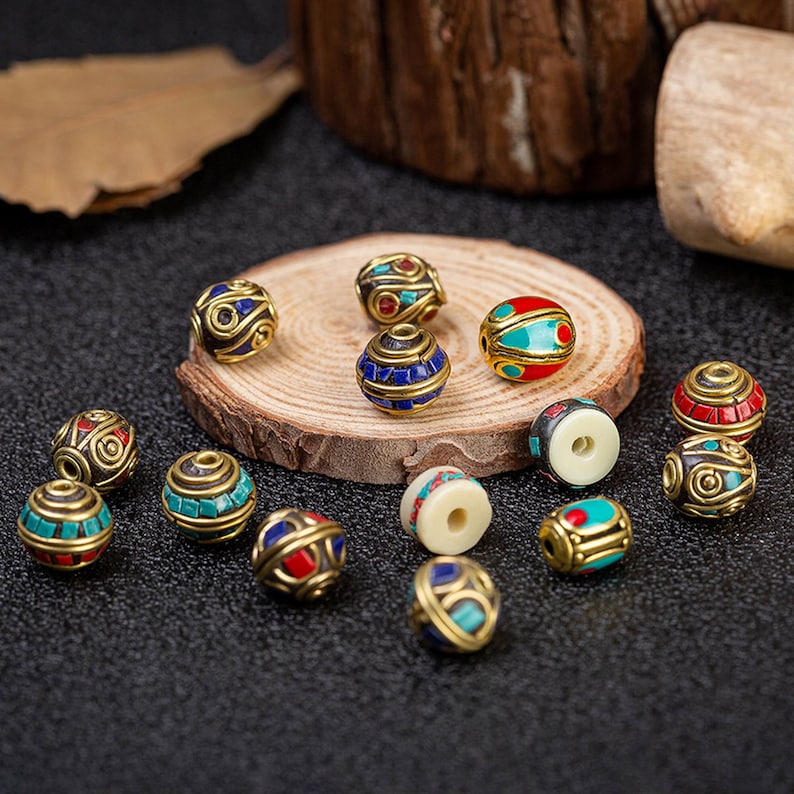 May include: Assortment of colorful round beads with intricate designs. The beads are made of metal and have a gold finish. They are decorated with blue, red, and green enamel. The beads are perfect for jewelry making or other craft projects.