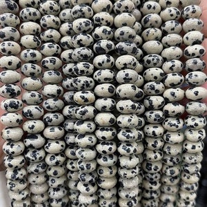 May include: A strand of black and white dalmatian jasper beads. The beads are oval shaped and have a speckled pattern.