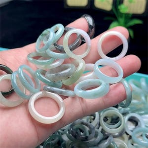 May include: A large pile of jadeite rings in various shades of green, white, and grey. The rings are smooth and polished, and they are all different sizes.