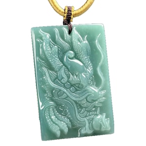 May include: A rectangular, light green jade pendant with a detailed carving of a dragon. The dragon is facing left, with intricate scales and features. The pendant is suspended from a gold-colored cord.