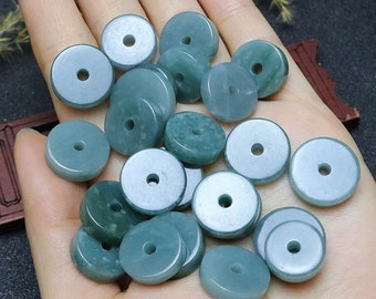 Può includere: Una collezione di perline di giada verde con un foro al centro. Le perline sono rotonde e piatte e sono disposte in un mucchio su una mano.