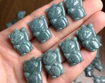May include: A collection of small, jade-colored Maneki Neko figurines, each with a raised paw, symbolizing good fortune. The figurines are carved with detailed features and are held in a hand, showcasing their size and color.