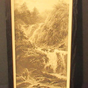 May include: A framed sepia-toned print of a waterfall in a forest. The image shows a cascading waterfall with trees and rocks surrounding it. The text "Avocadh Falls" is printed at the bottom of the image.