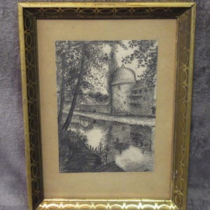 May include: A framed charcoal drawing depicting a stone tower with a domed roof situated beside a body of water, surrounded by trees. The artwork is encased in a rectangular gold-toned frame featuring a repeating oval pattern along the border.