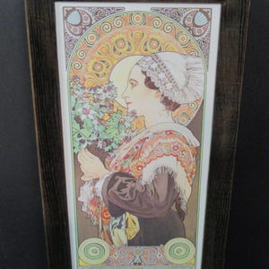 May include: A framed print featuring an illustration of a person in profile wearing a white lace cap and a patterned shawl, holding a bouquet of flowers. The artwork is surrounded by a decorative circular border with orange, yellow, and green tones.
