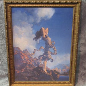 May include: A framed print featuring a woman with flowing hair and draped clothing, set against a backdrop of mountains, a lake, and a blue sky with clouds. The frame is gold-colored with ornate detailing. The artwork evokes a classical, romantic theme.