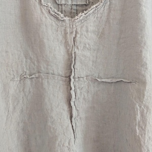 May include: Light blue linen top with a frayed neckline and seams. The top features a V-neck and a small tag that reads "BREATHE". The fabric has a slightly wrinkled texture.