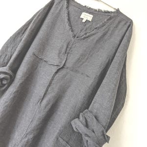 May include: A gray long-sleeved shirt with a V-neck and frayed edges. The shirt has a relaxed fit, two front pockets, and the sleeves are rolled up. The label reads "breathe".