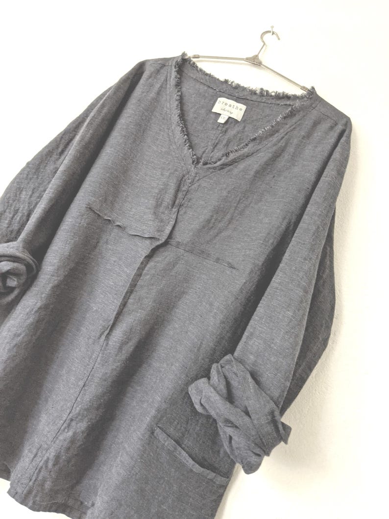 May include: A gray long-sleeved shirt with a V-neck and frayed edges. The shirt has a relaxed fit, two front pockets, and the sleeves are rolled up. The label reads "breathe".