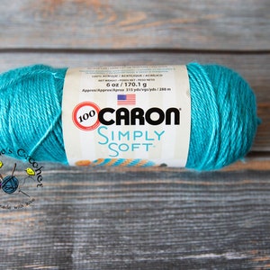 Può includere: Un gomitolo di filato Caron Simply Soft di colore turchese. L'etichetta riporta "100% Acrilico, 6 oz/170,1 g, Circa 315 yds/288 m".