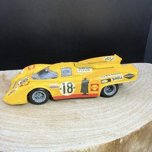 Peut inclure: Un modèle réduit de voiture de course jaune portant le numéro 18 sur le capot et les côtés. La voiture présente divers autocollants de sponsors dont Shell, Goodyear et Marchal, ainsi que le texte David Piper et un graphique silhouette noir.