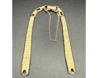 May include: A gold-tone metal watch band featuring a series of rectangular, textured links that taper slightly toward the ends. The band includes a secure clasp mechanism at the top and a delicate, thin safety chain attached to prevent accidental loss.