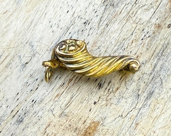 May include: A gold-toned metal charm shaped like a cornucopia, featuring a spiraled, ribbed texture along its body and a small circular loop attached to the wider end for hanging. The object has a polished finish with visible metallic highlights.