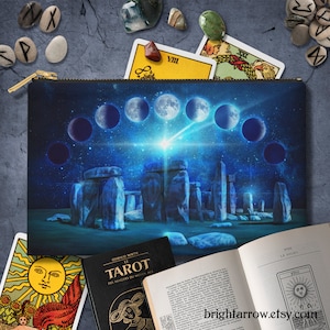 May include: A blue zippered pouch with a design of Stonehenge and a starry night sky with a crescent moon and a shooting star. The pouch is surrounded by tarot cards and crystals.