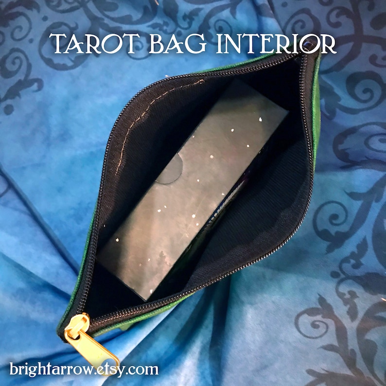 May include: A green tarot bag with a gold zipper is open, revealing a black tarot deck inside. The bag is lined with black fabric. The text "TAROT BAG INTERIOR" is printed on the bag.