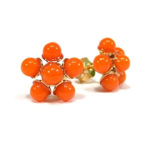 Puede incluir: Un par de pendientes de color naranja en forma de flor con detalles dorados.