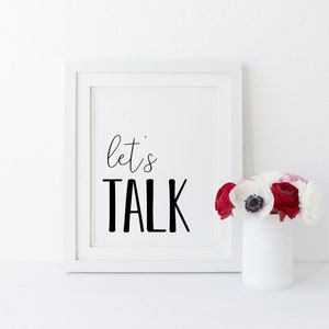 May include: White framed print with black text that reads "let's TALK" against a white background. A vase with white and red flowers sits in front of the print.