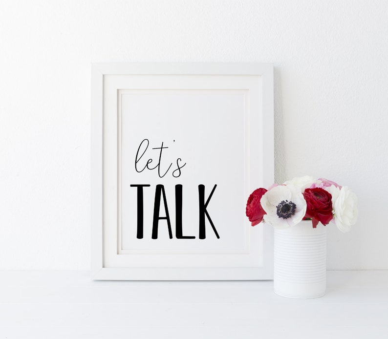 May include: White framed print with black text that reads "let's TALK" against a white background. A vase with white and red flowers sits in front of the print.