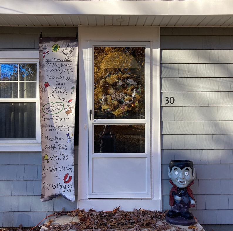 May include: A festive front door scene with a white door, a Christmas list banner, and a vampire-themed planter. The banner lists holiday items like snow, stockings, and sleigh bells. A wreath adorns the door, and the house number 30 is visible.