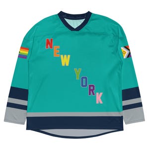 Peut inclure: Maillot de hockey teal avec le mot "NEW YORK" en couleurs arc-en-ciel. Le maillot a un col en V, des accents bleu marine et gris sur les manches et le bas, et des drapeaux arc-en-ciel et de la fierté progressiste sur les manches.