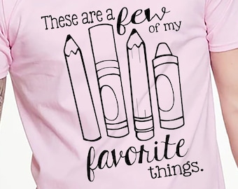 Puede incluir: Camiseta rosa con un gráfico negro de lápices y crayones. El texto dice "Estas son algunas de mis cosas favoritas."